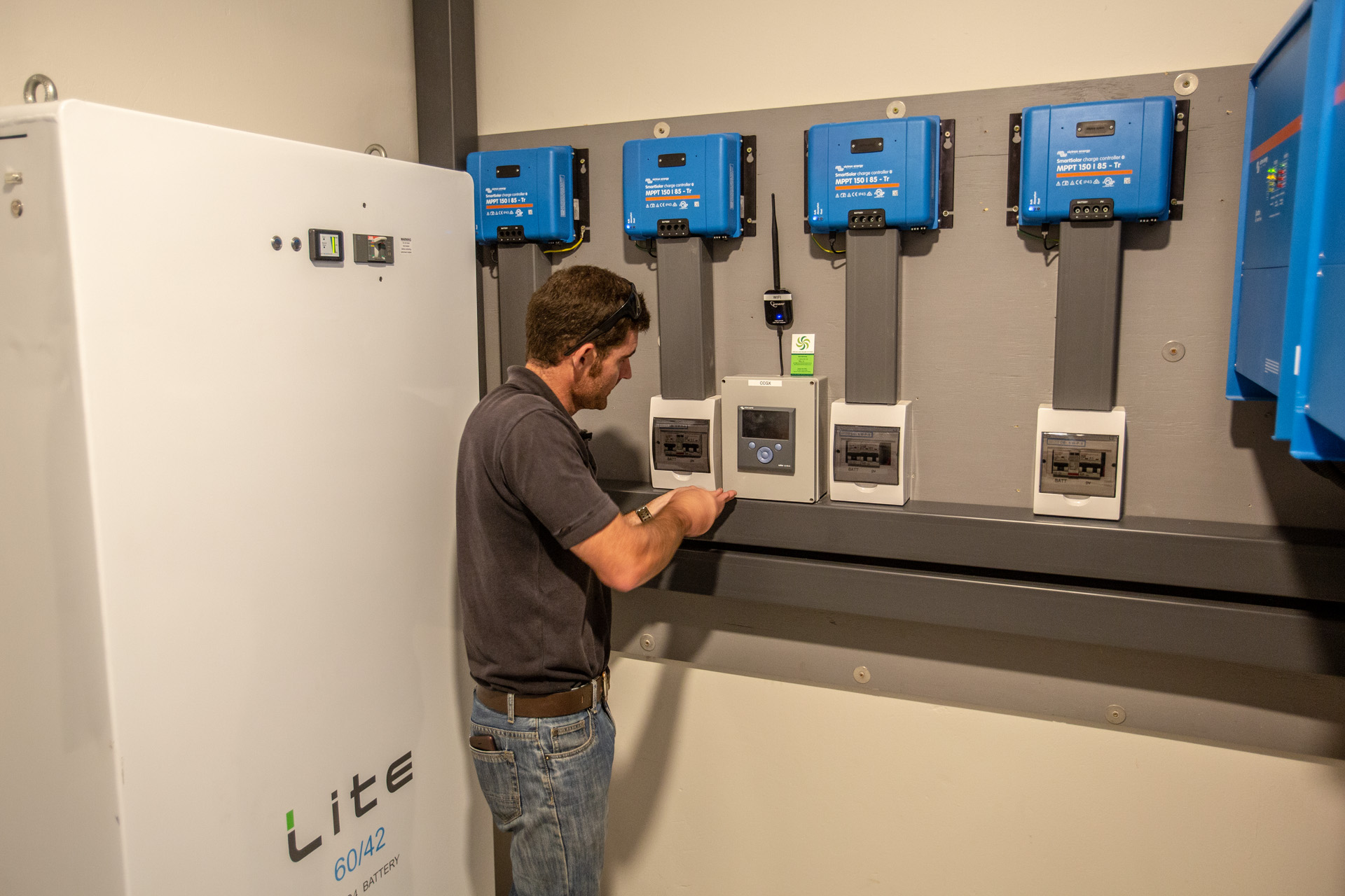 A solar technician performing quality and compliance checks on a multi-controller solar power installation with lithium battery storage.
