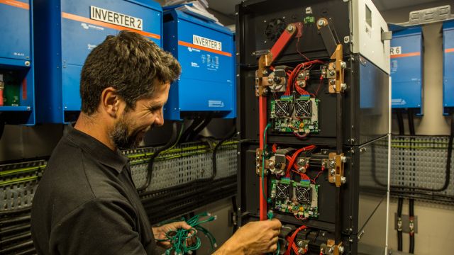 Technician connecting battery management system wiring and inverter integration inside a locally engineered solar power room